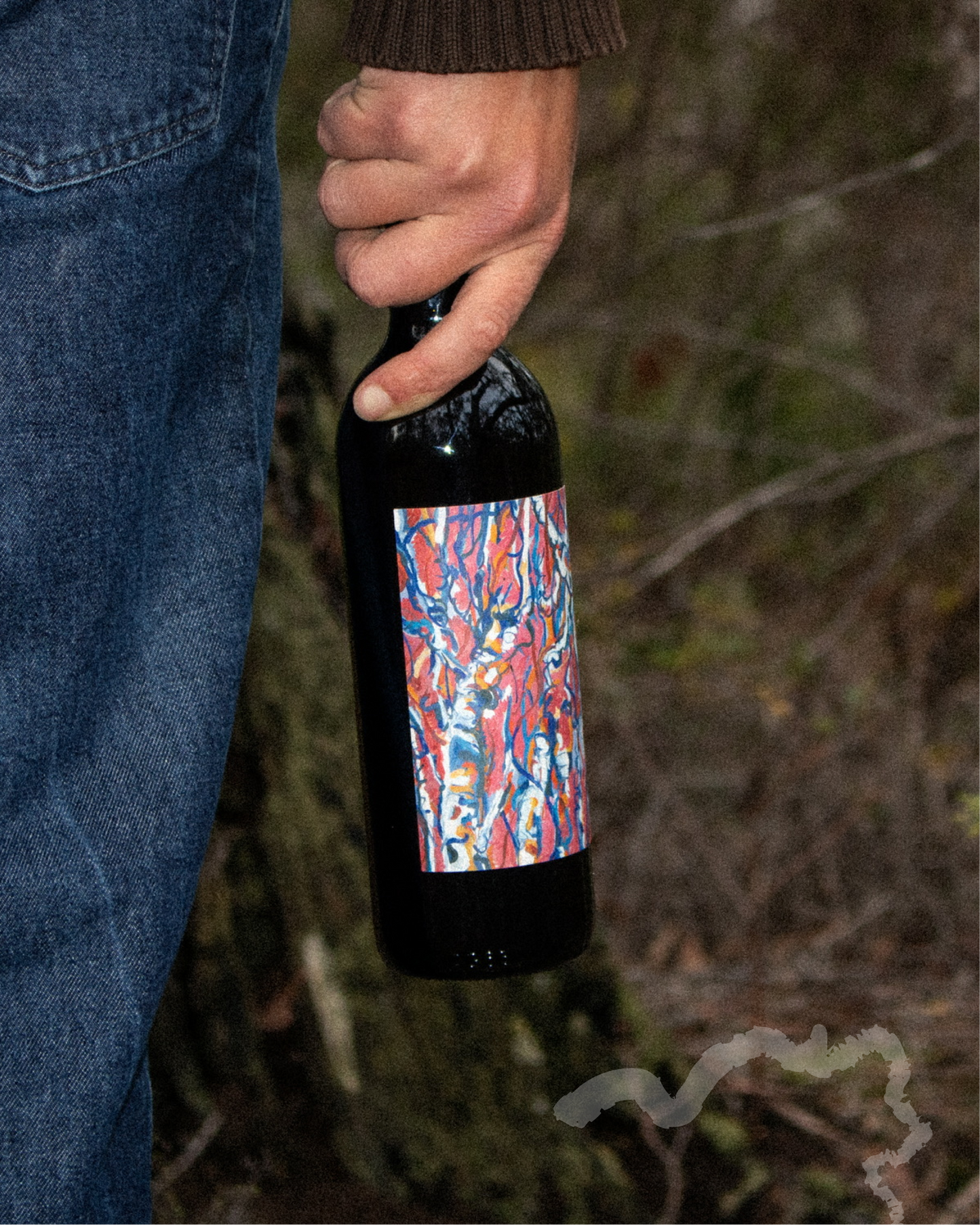 Hand holding a wine bottle with a colorful label against a natural background